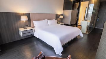Una habitación de hotel moderna con una cama grande, dos mesitas de noche con lámparas, un cabecero de madera y un box de ducha de vidrio.