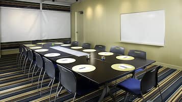 A conference room with a long table, chairs, a whiteboard, and a projector screen.