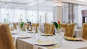 Un comedor formal con mesas dispuestas para una comida, con sillas en tonos dorados y manteles blancos.
