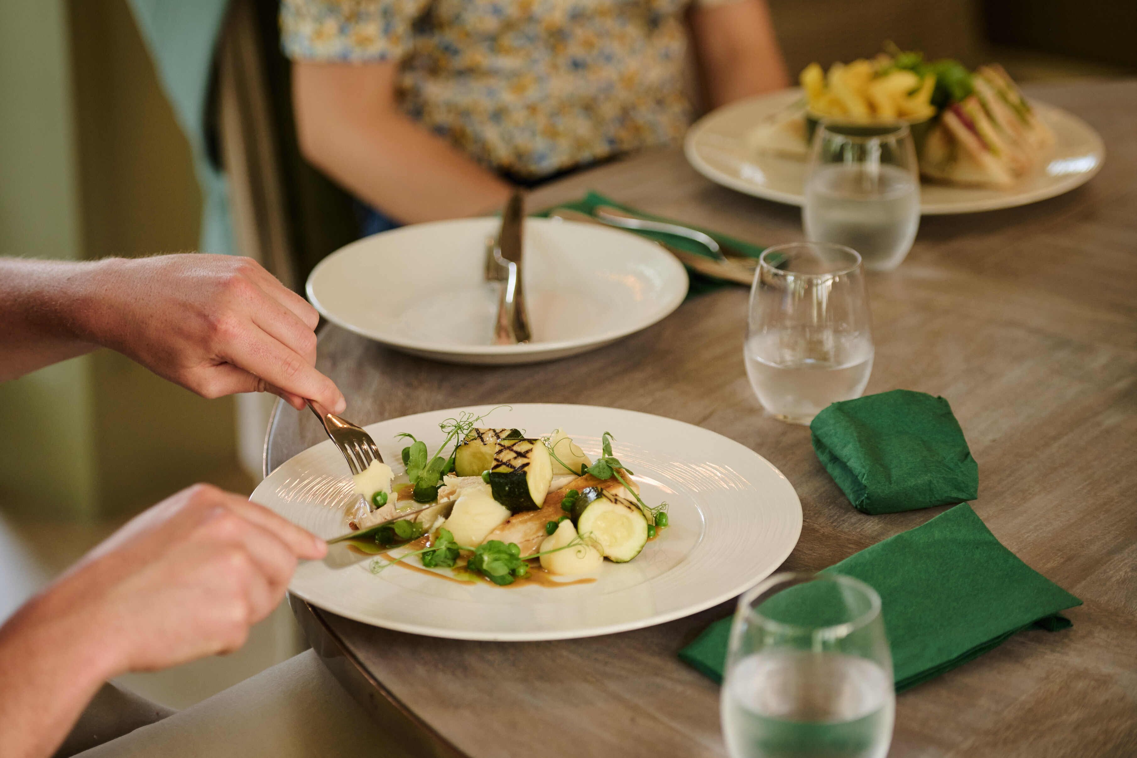 Una mesa de comedor con platos de comida, un tenedor, un cuchillo y un vaso de agua.