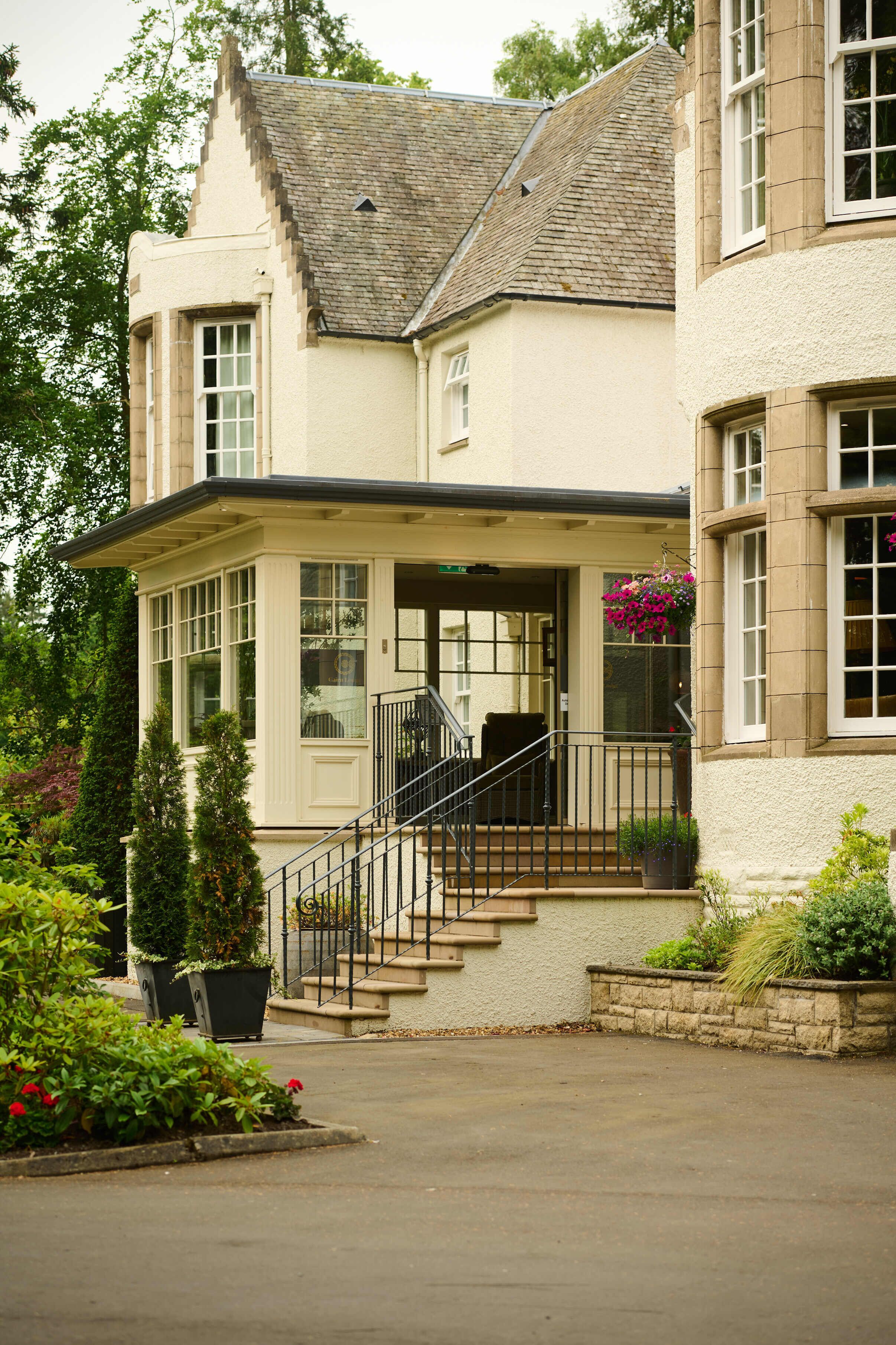 A two-story building with a white exterior, a balcony with a black railing, and a small porch area.