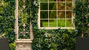Une terrasse de jardin avec des meubles en osier, une grande fenêtre en arc de cercle et une végétation luxuriante.