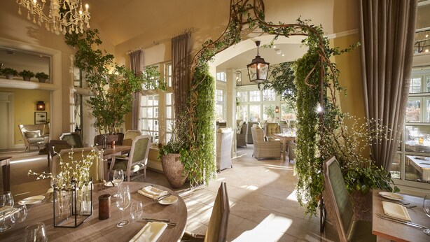 Un espace repas avec des tables dressées pour le repas, entouré d’une végétation luxuriante et agrémenté d  ’une arche décorative.