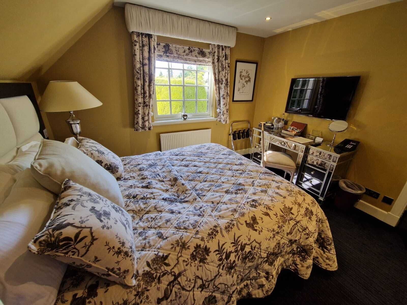 A bedroom with a bed, a desk, a chair, a TV, and a window with curtains.