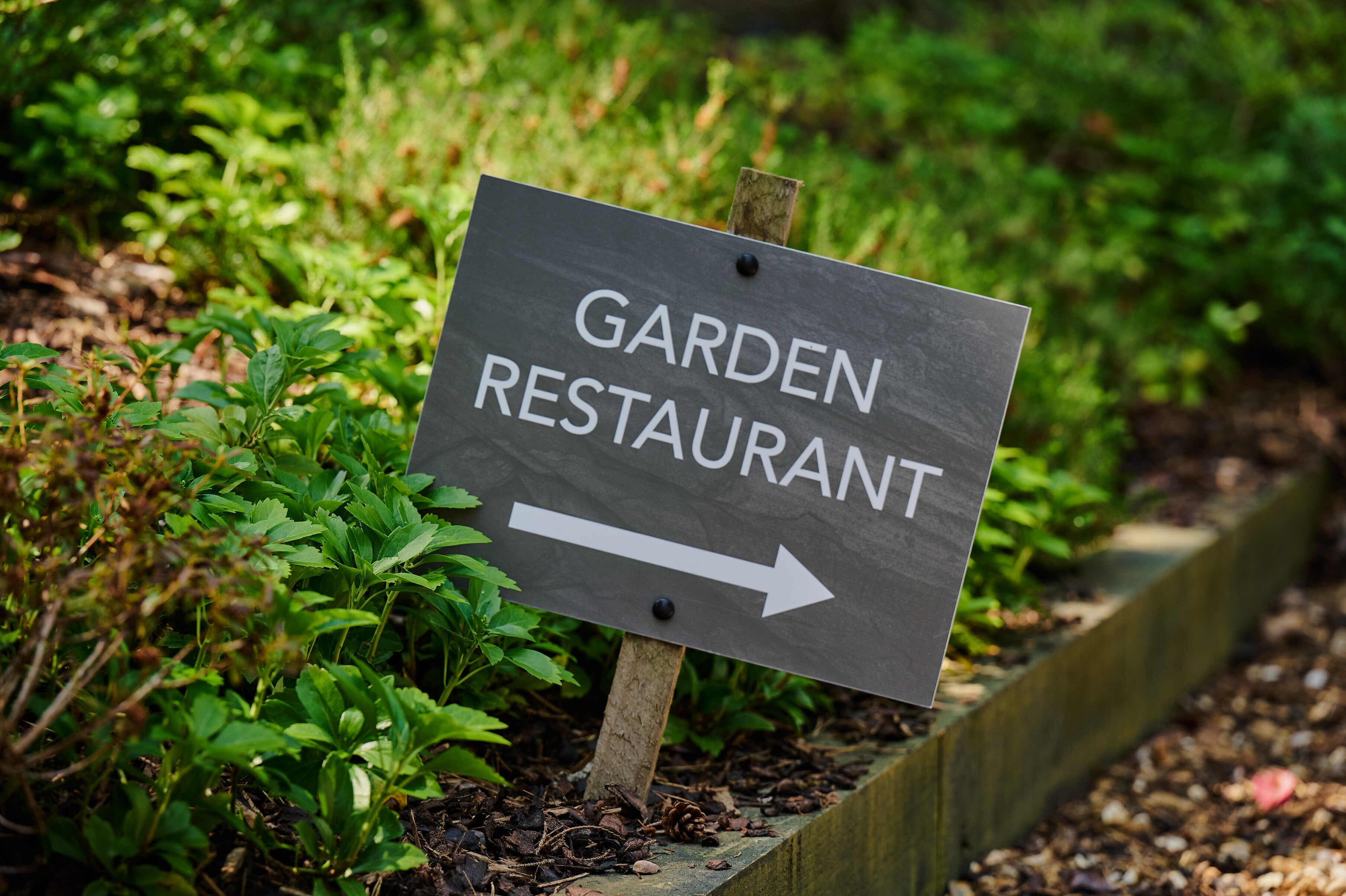 A sign for a garden restaurant with an arrow pointing to the right.