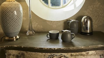 Una mesa de estilo antiguo con una lámpara, un jarrón con flores, un hervidor y una taza.