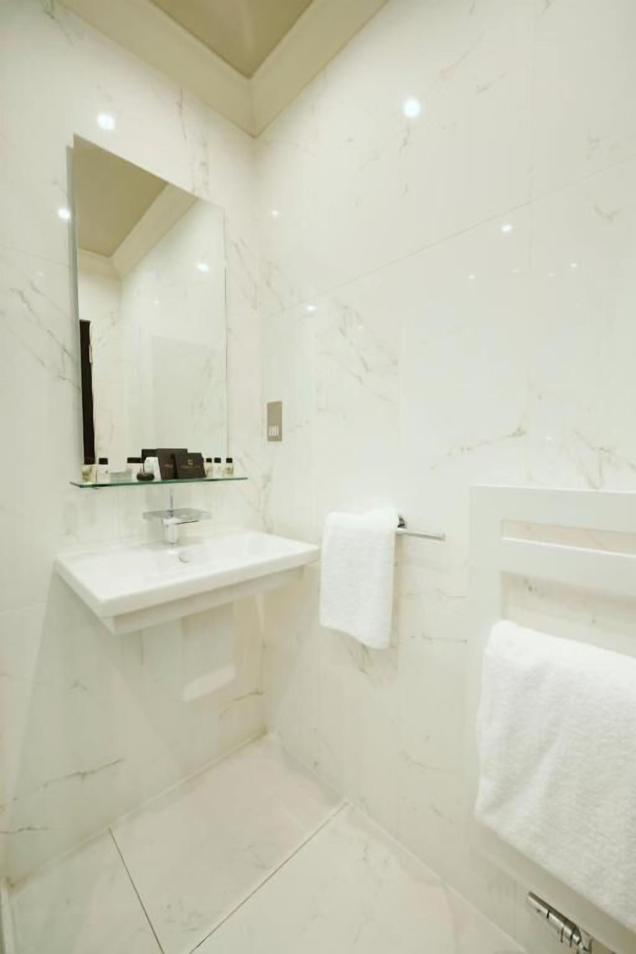 A modern bathroom with a white marble sink, a large mirror, and a towel rack.