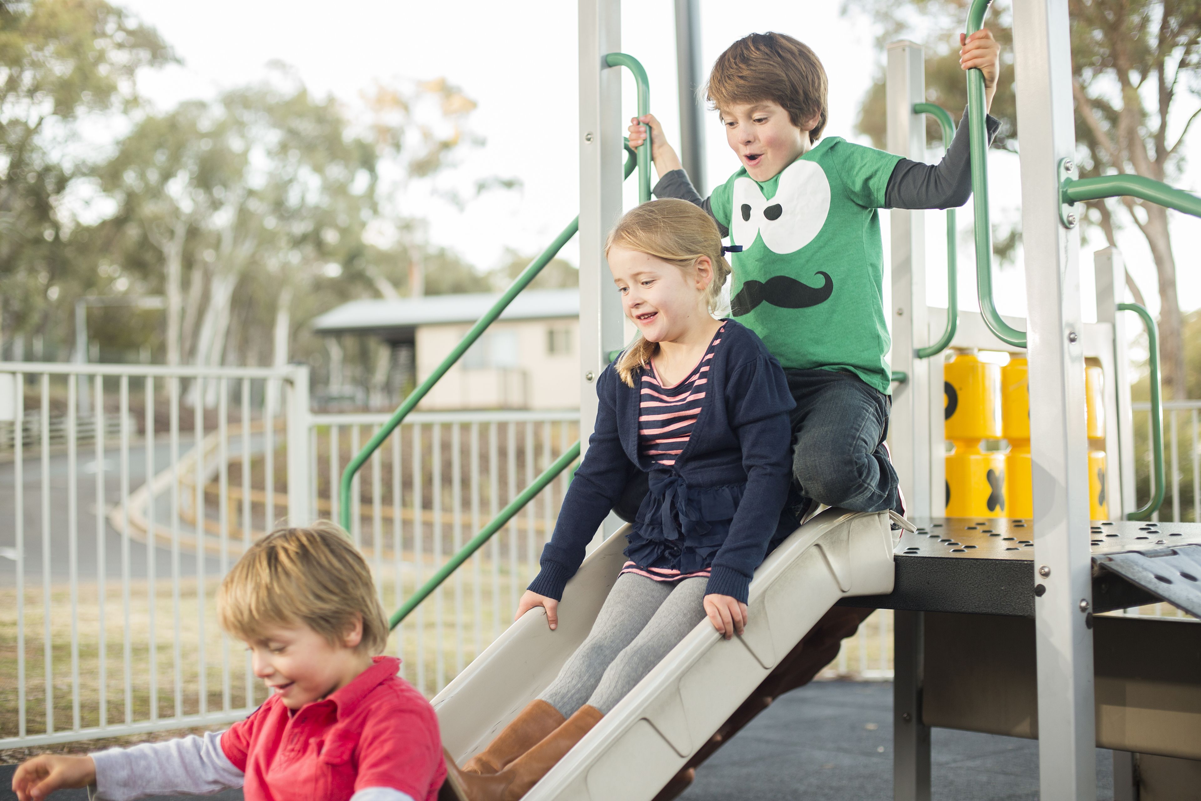Children playing on a playground with a slide and climbing structure.