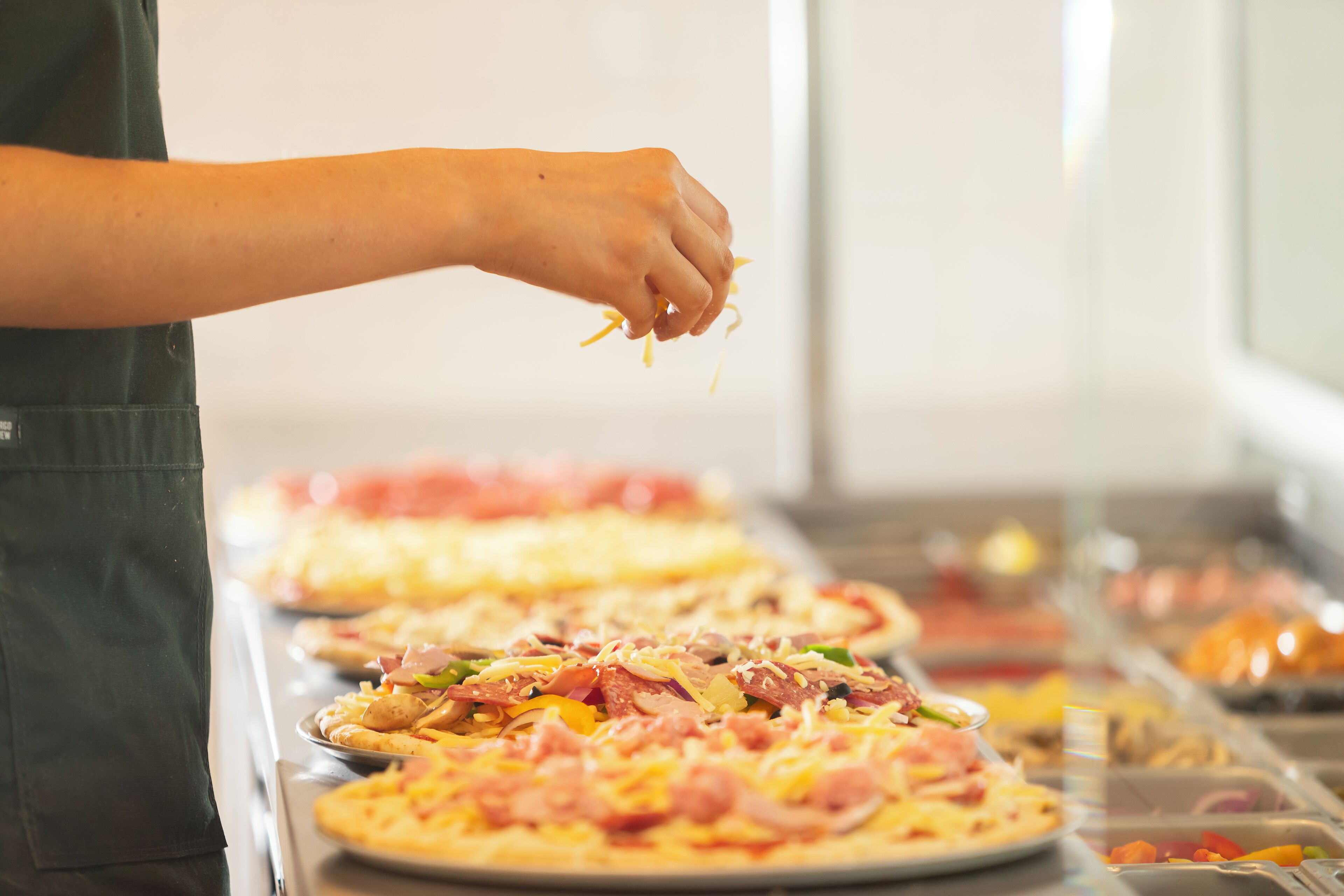 Uma pessoa preparando pizzas com diversos ingredientes.