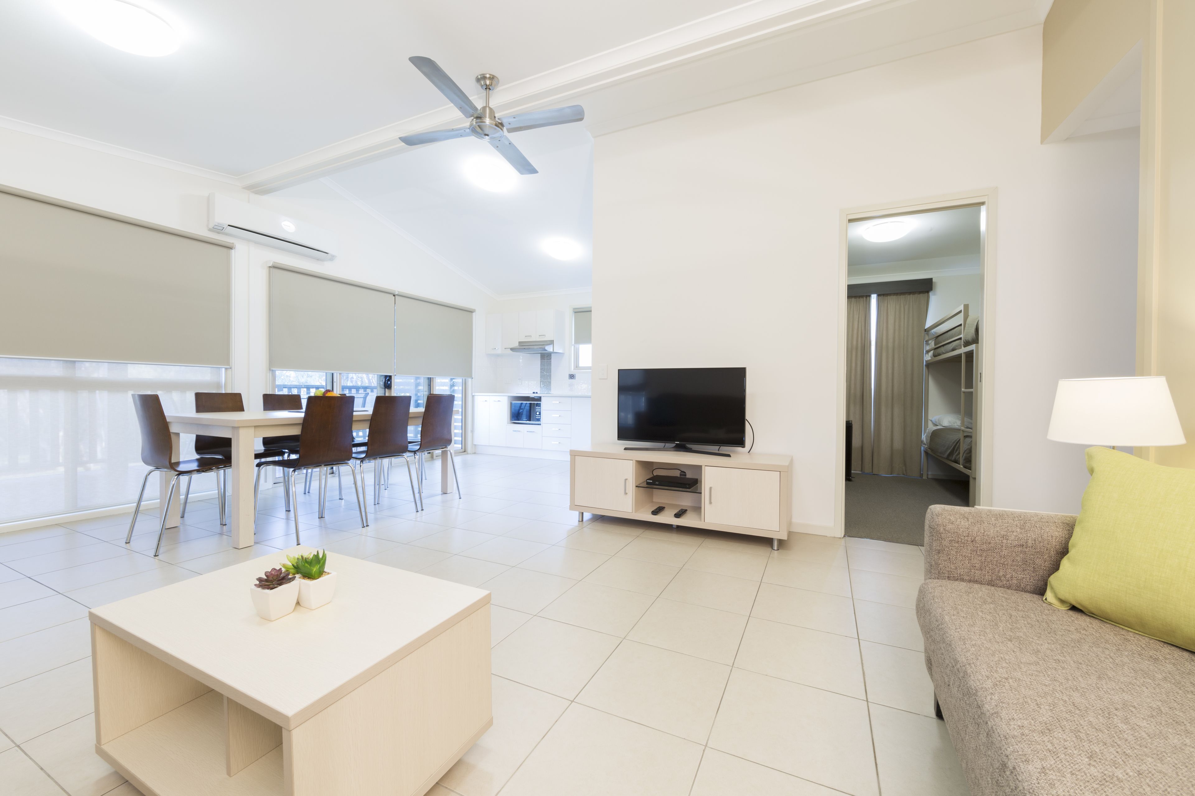 A modern living room with a flat-screen TV, a sofa, a coffee table, and a dining area with chairs and a table.