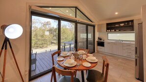 A dining area with a table set for four, a modern kitchen with wooden cabinets, and a large sliding glass door leading to an outdoor deck. - Alivio Tourist Park Canberra (O'Connor)