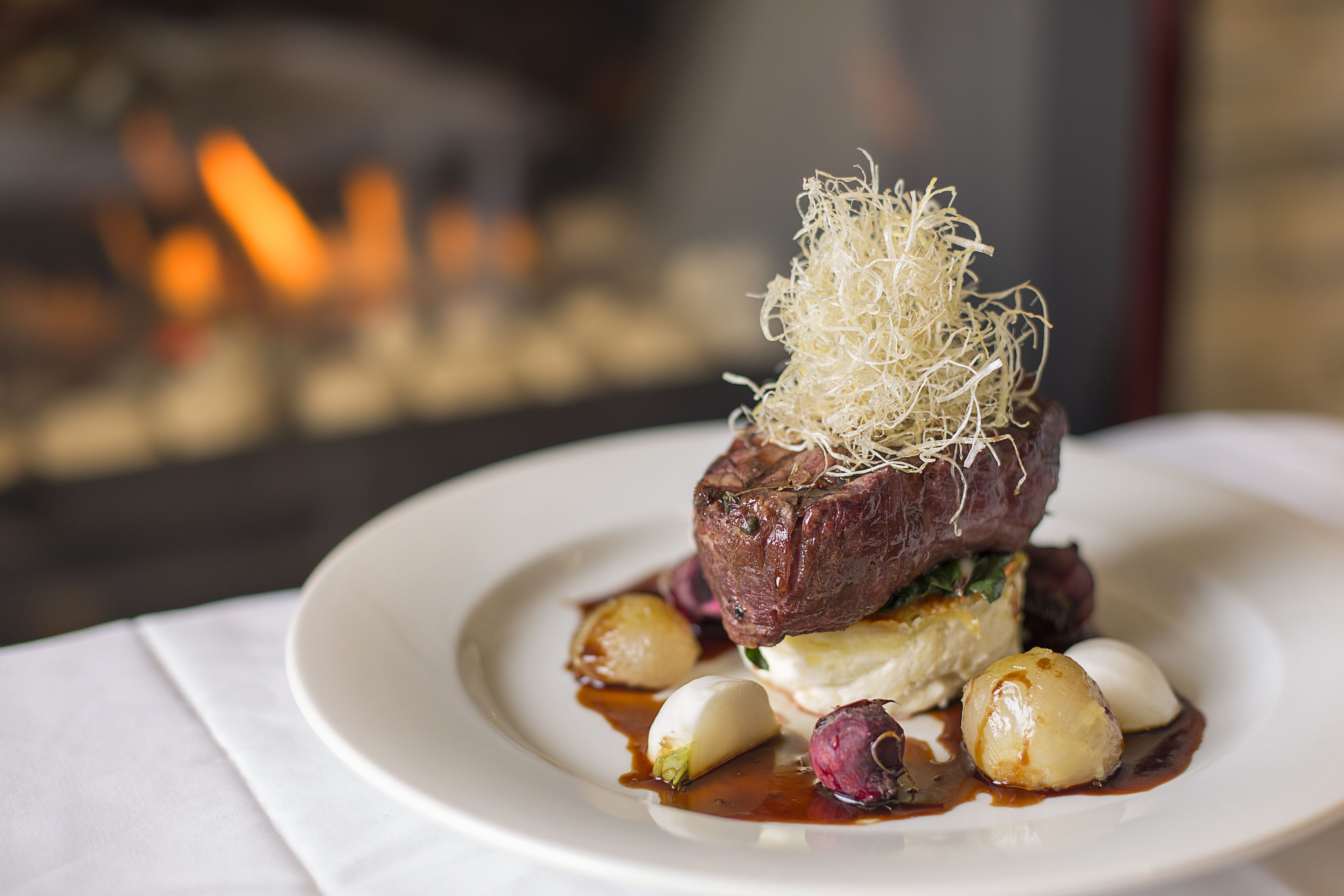 Un plato emplatado con carne, verduras y un adorno decorativo sobre una vajilla blanca.