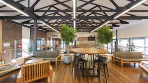 A spacious indoor area with a high ceiling, wooden flooring, and a central round table surrounded by stools. There are seating areas with sofas and a bench. - Alivio Tourist Park Canberra (O'Connor)