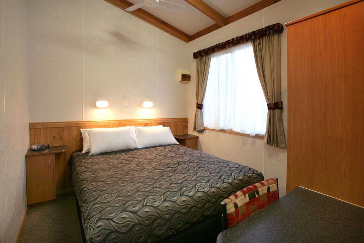 Een slaapkamer met een bed, nachtkastjes, een raam met gordijnen en een plafondventilator.