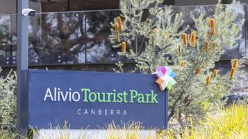 A sign for Alivio Tourist Park in Canberra with a clear view of the surrounding vegetation.
