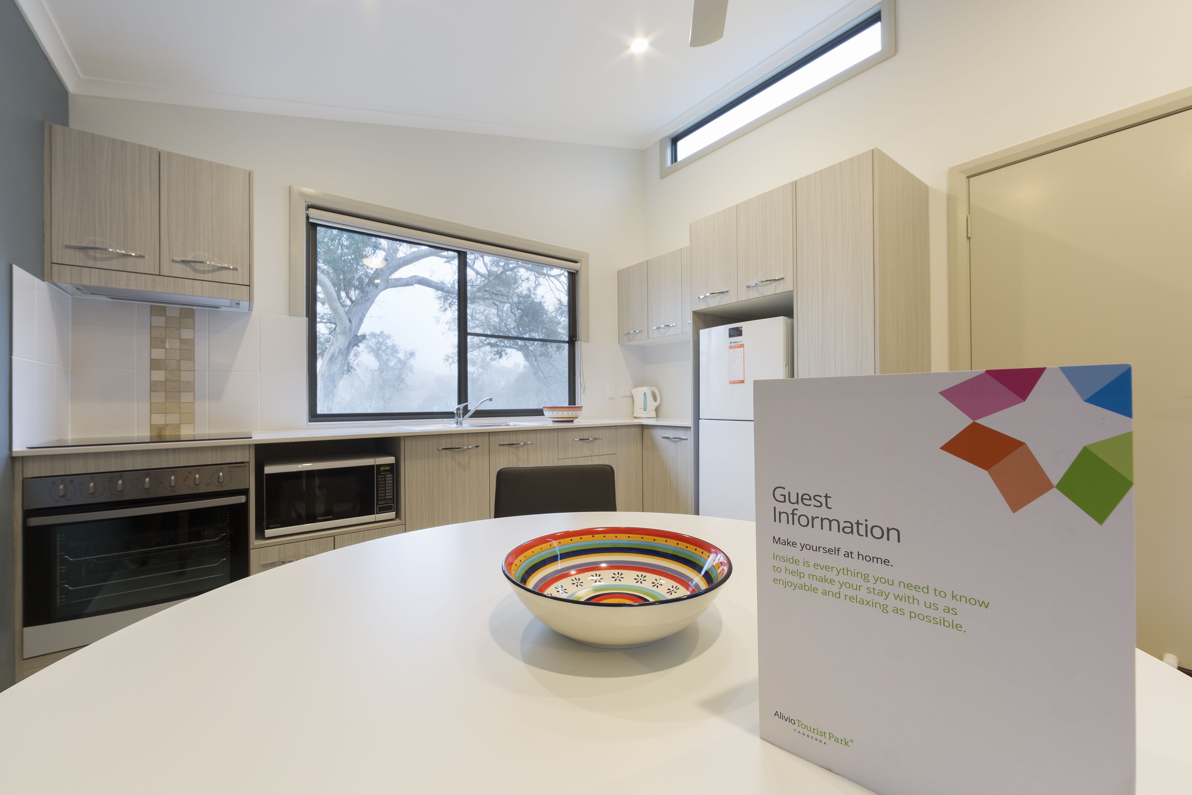 A modern kitchen with a large window, a microwave, an oven, and a bowl on the counter.