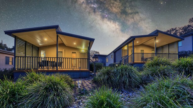 Two modern cabins with large balconies, surrounded by native vegetation, under a starry night sky. - Alivio Tourist Park Canberra (O'Connor)