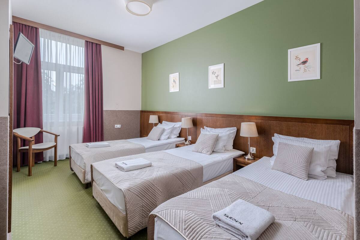 A hotel room with three beds, a wooden headboard, a desk, and a chair.