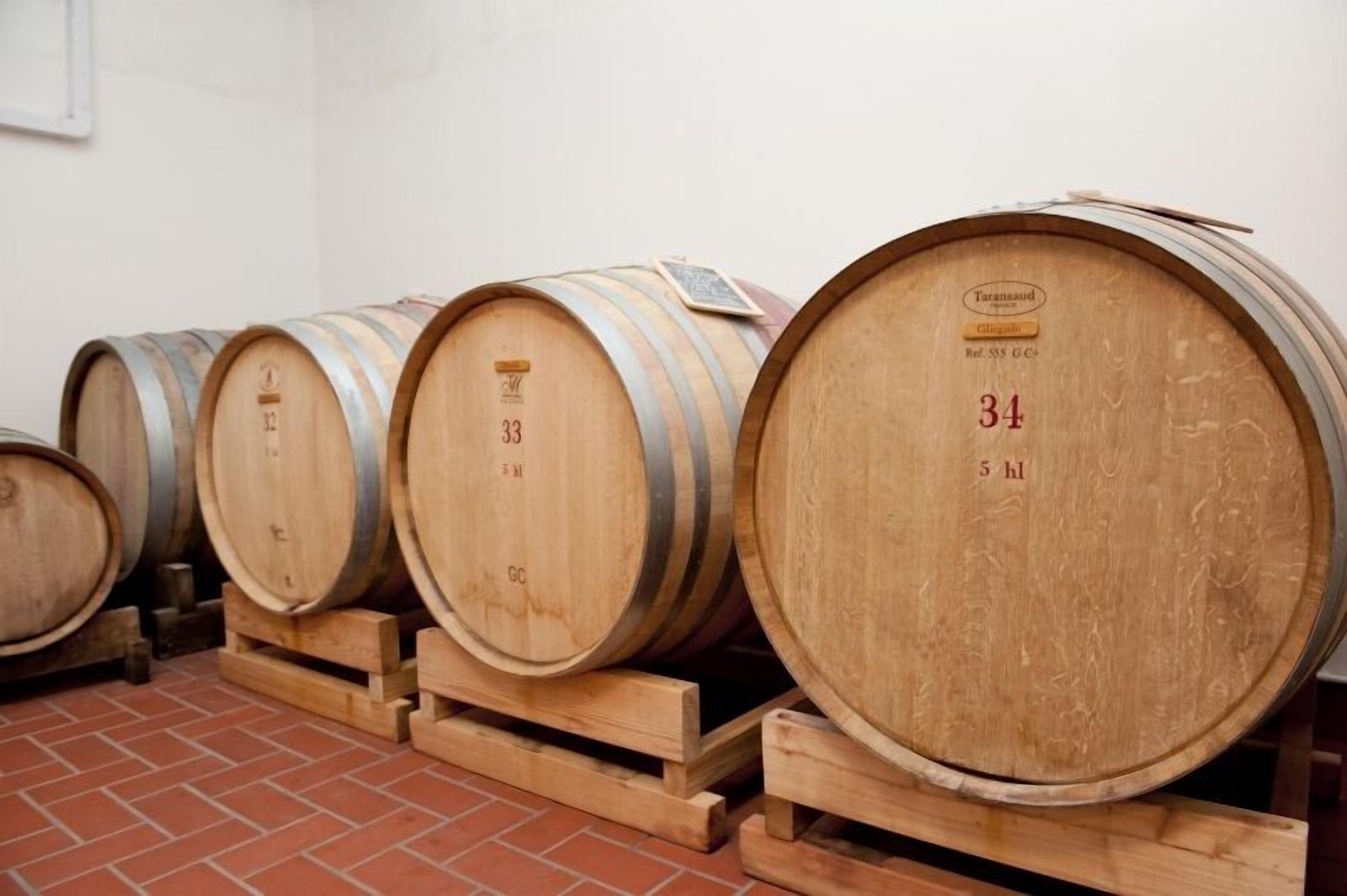 Wooden wine barrels stacked on wooden pallets in a room with a tiled floor.