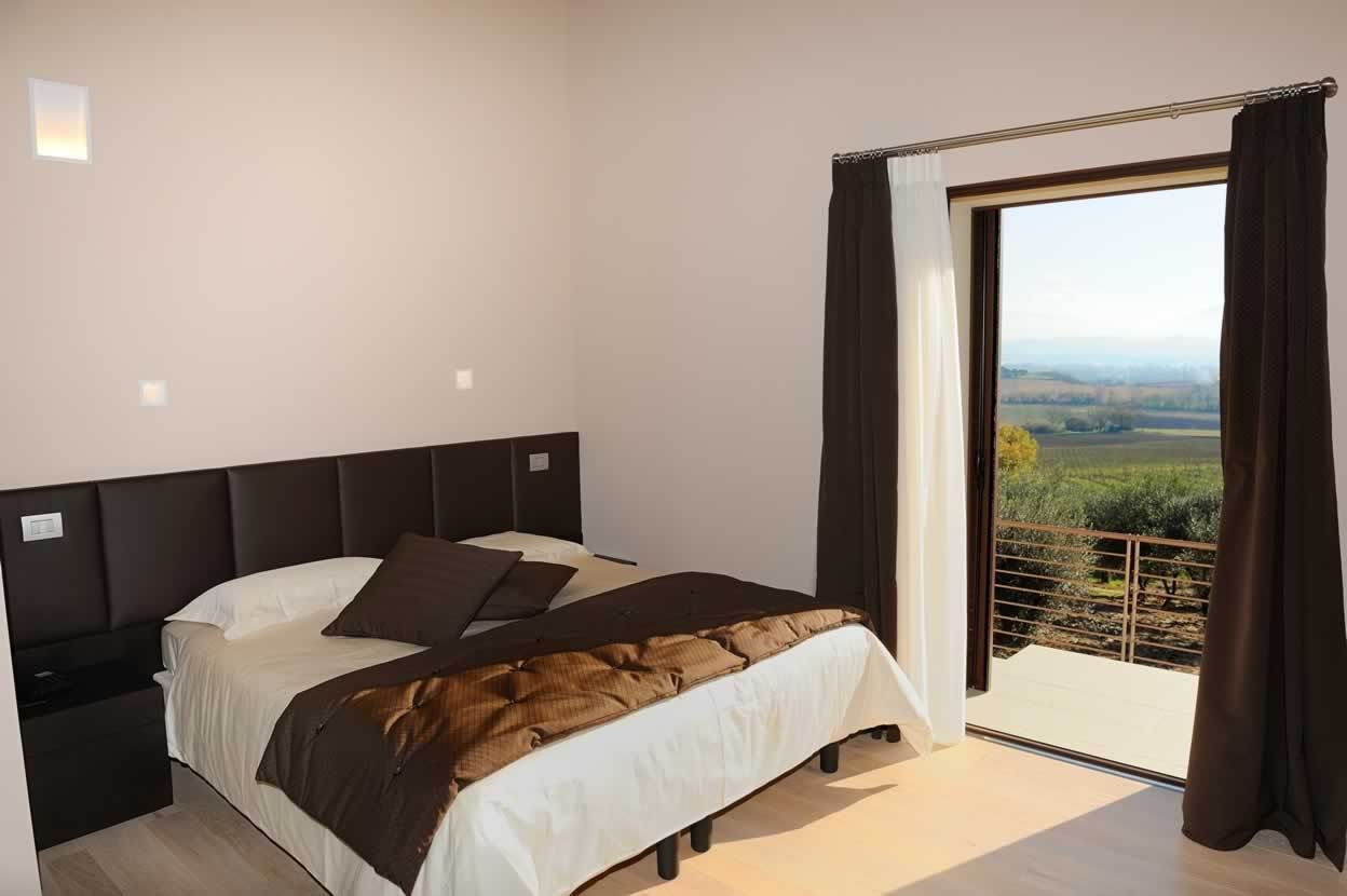 A bedroom with a bed, a nightstand, and a view of a landscape through a large window.