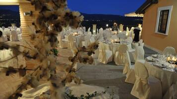An outdoor dining area with round tables set for a meal, surrounded by chairs with white covers.