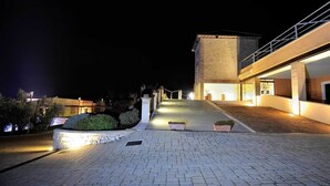 Vista noturna de um edifício moderno com entrada pavimentada e escadaria que leva ao nível superior.