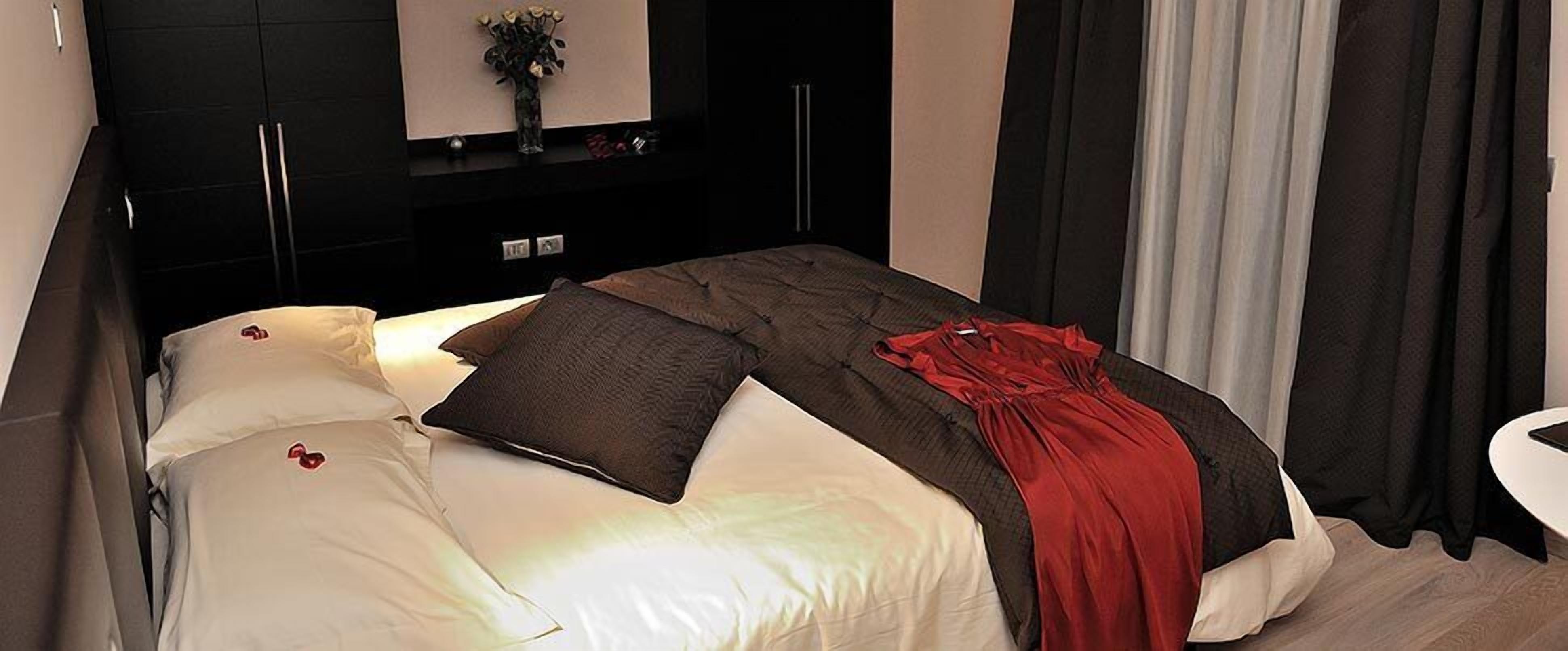 A neatly made bed with a red and black blanket, a white pillow, and a dark pillow.