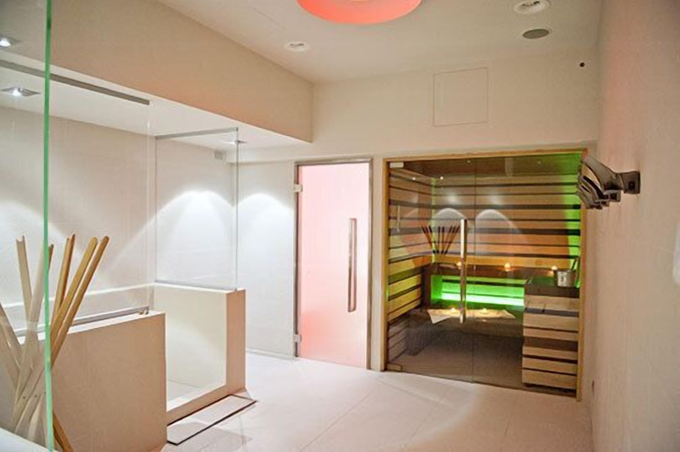 A modern hotel room with a glass partition, a wooden cabinet, and a staircase with green lighting.