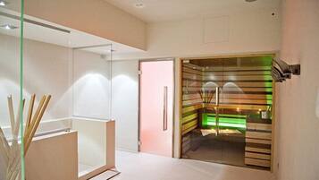 A modern hotel room with a glass partition, a wooden cabinet, and a staircase with green lighting.