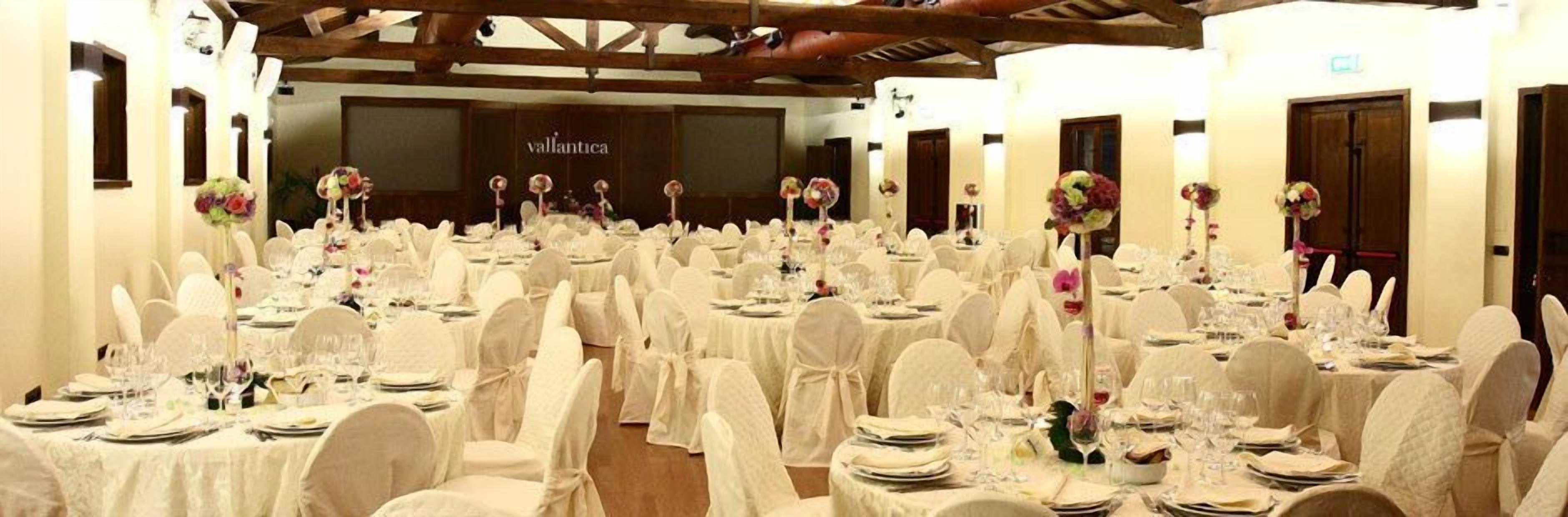 A banquet hall with round tables set for a formal event, featuring white tablecloths and floral centerpieces.