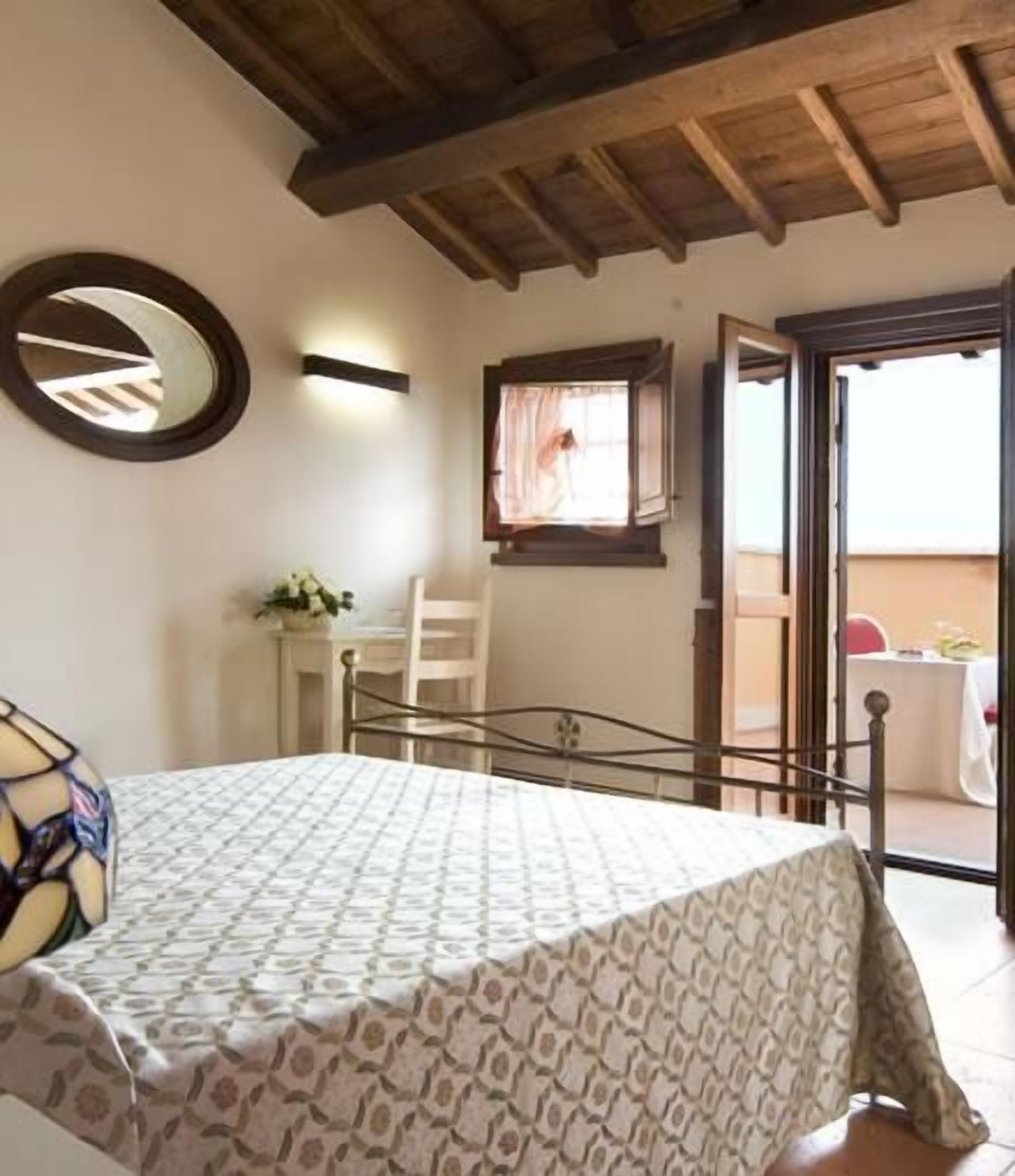 Een slaapkamer met een bed, een spiegel, een raam met gordijnen en een balkon met een tafel en stoelen.