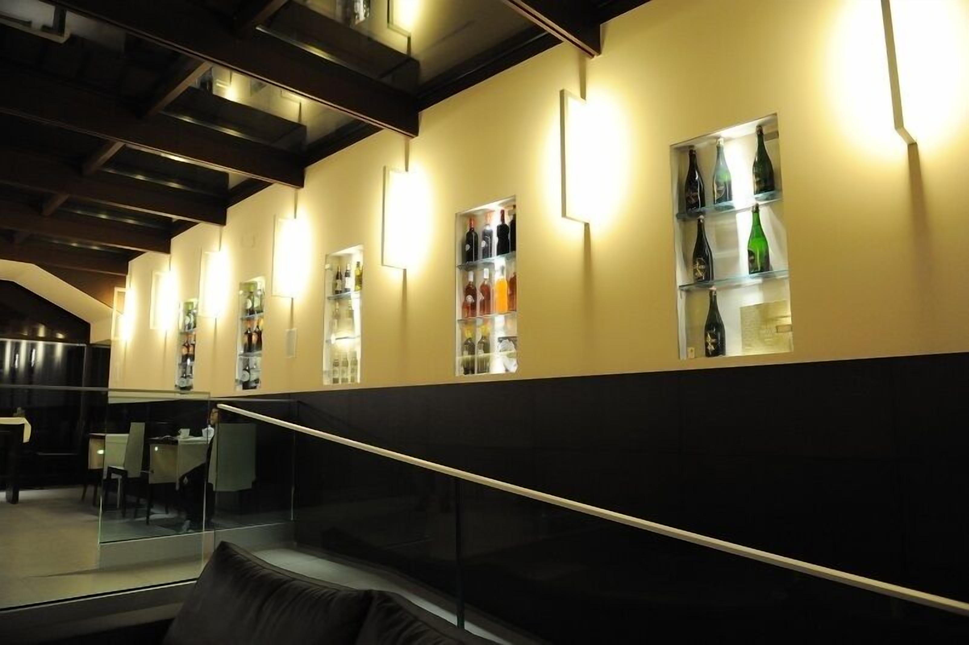 A modern interior with a staircase, glass railings, and shelves displaying bottles.