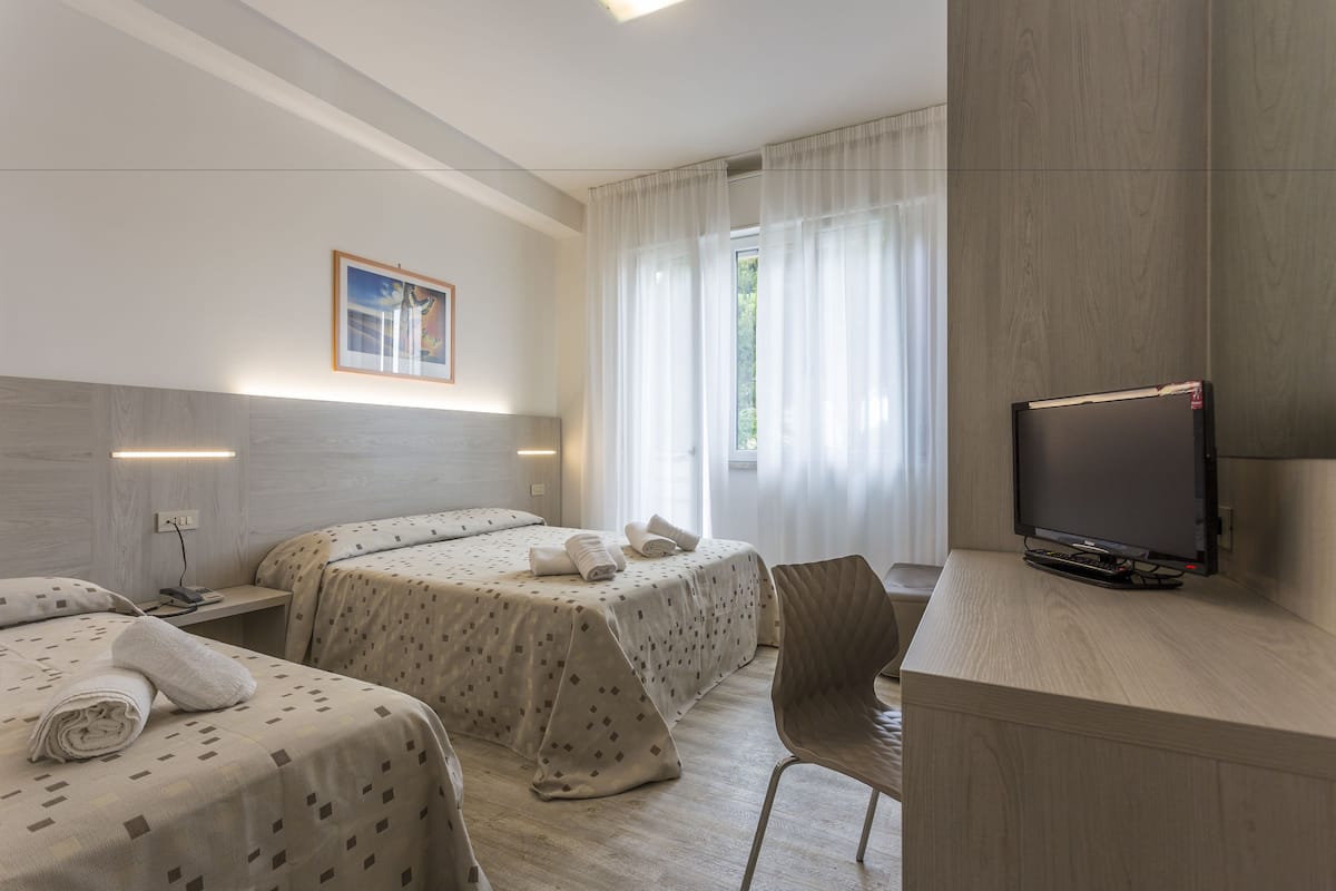Habitación de hotel con dos camas, televisor, escritorio y una silla.