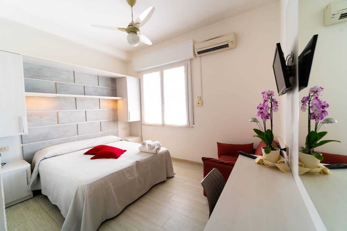 Habitación de hotel moderna con cama, escritorio, silla, televisor y ventilador de techo.