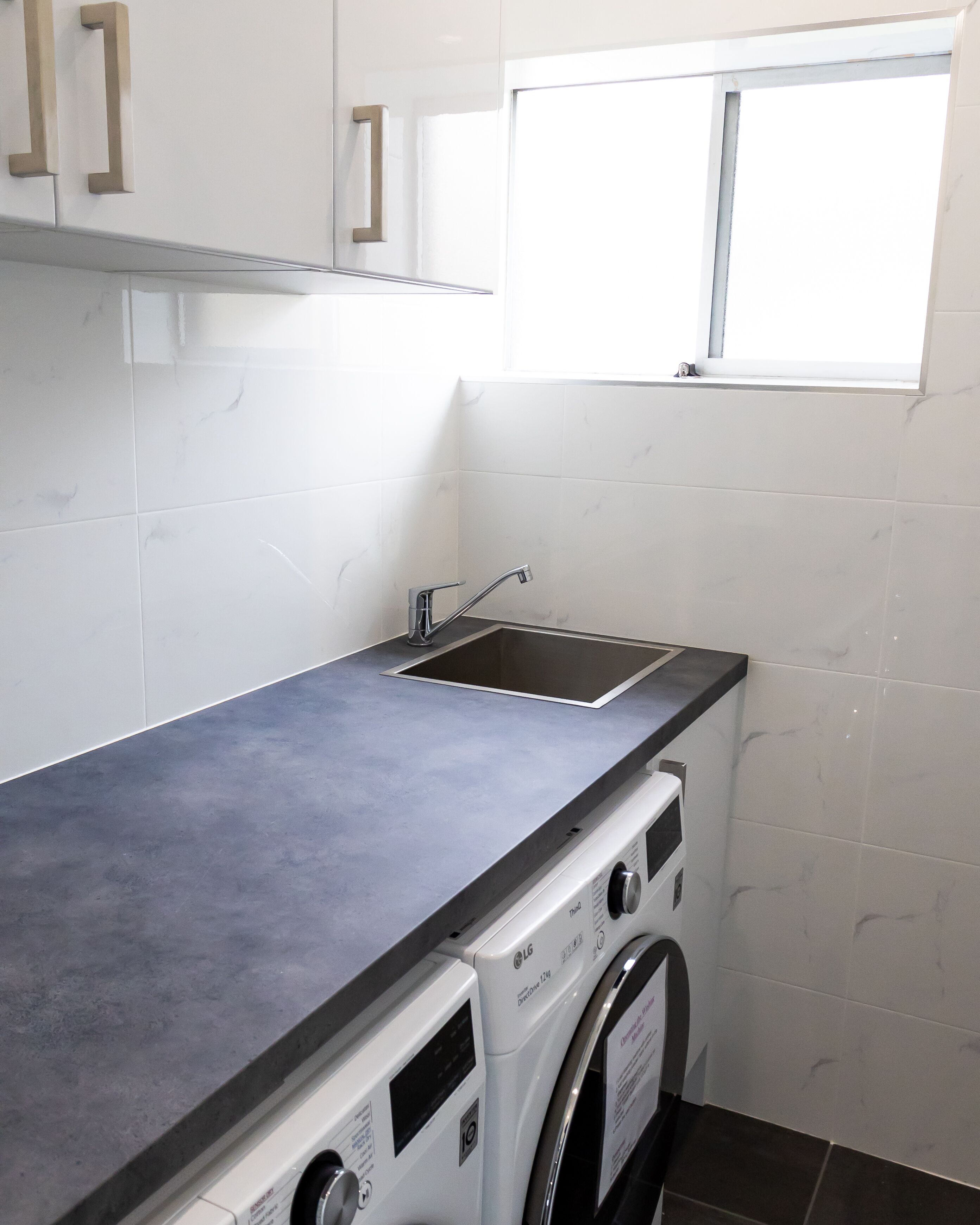 A compact laundry area with a washing machine, a sink, and a window.