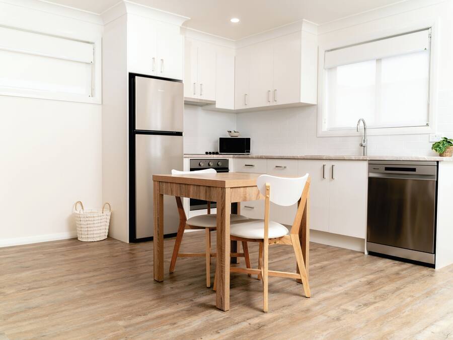 Una cocina moderna con armarios blancos, una mesa de madera y un lavavajillas de acero inoxidable.