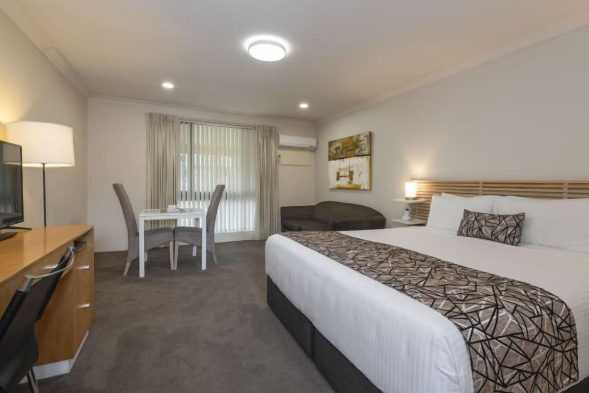 Une chambre d’hôtel comprenant un lit, un bureau avec une chaise, une télévision, une fenêtre avec des rideaux et un tableau au mur.