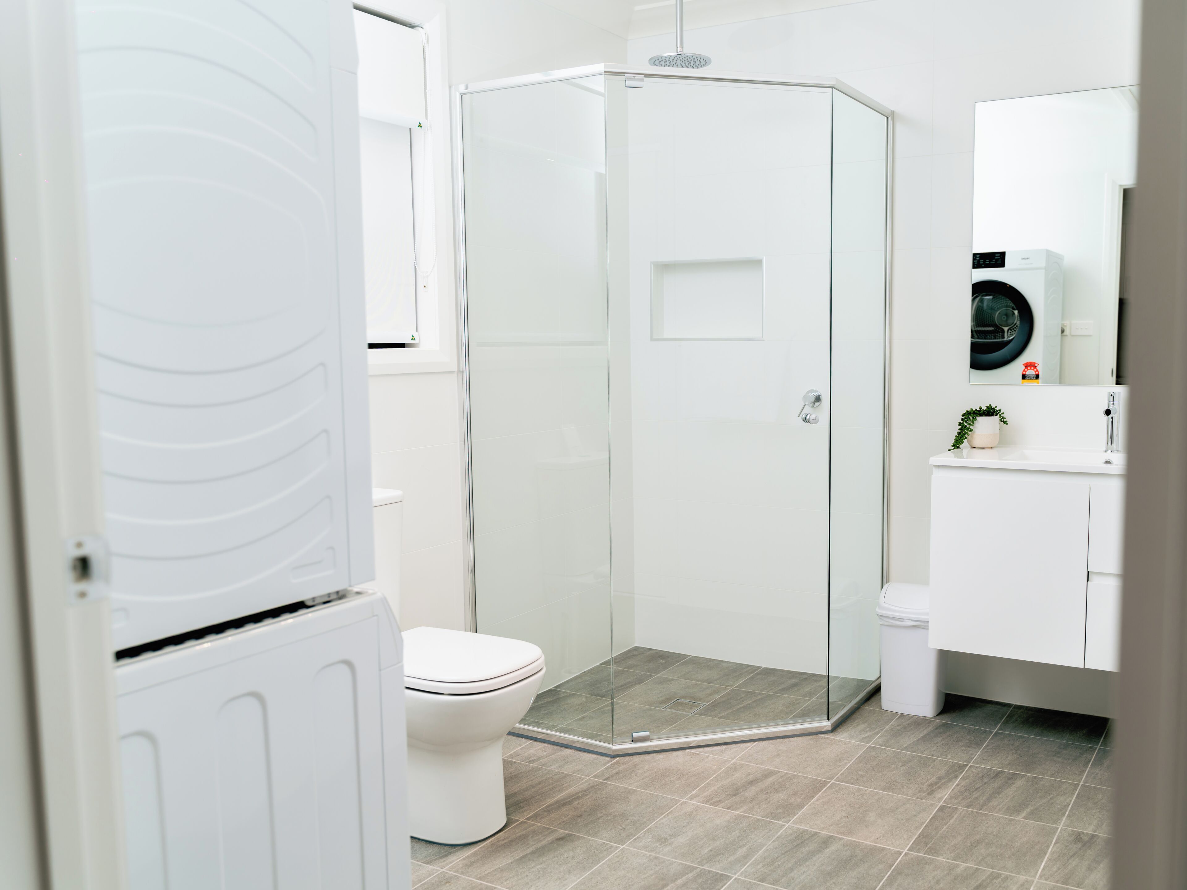 A modern bathroom with a glass-enclosed shower, a toilet, and a sink with a mirror above.