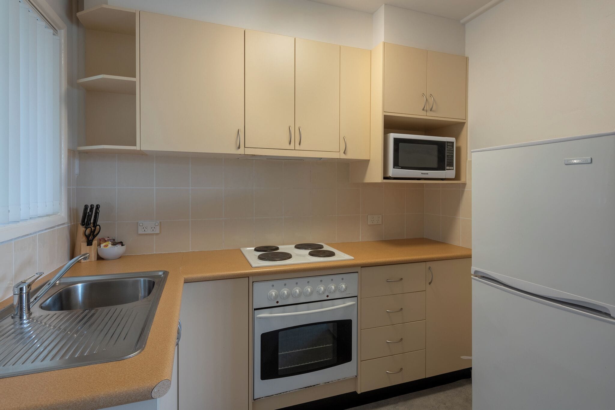 A kitchen with beige cabinets, a microwave, a stove, a sink, and a refrigerator.