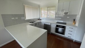A modern kitchen with grey cabinetry, a white countertop, and a built-in dishwasher. - Zig Zag Motel (Lithgow)