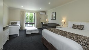 A hotel room with a large bed, a smaller bed, a sofa, a desk, and a chair. There is a window with curtains, a lamp, and a framed picture on the wall. - Zig Zag Motel (Lithgow)