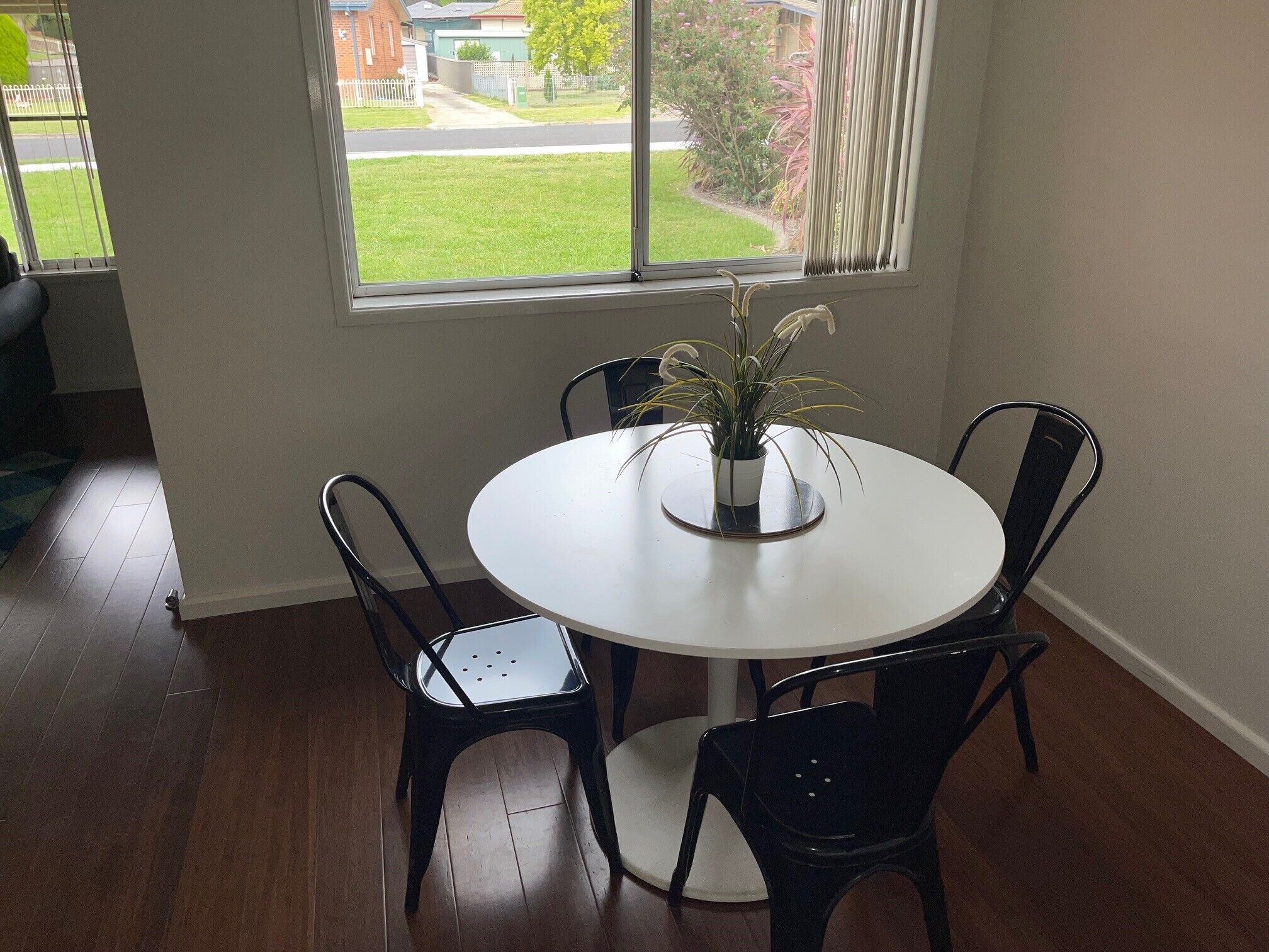 A dining area with a round white table, four black chairs, and a potted plant.