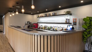 A modern bar area with a curved counter, multiple bottles, a coffee machine, and a tablet. - Zig Zag Motel (Lithgow)