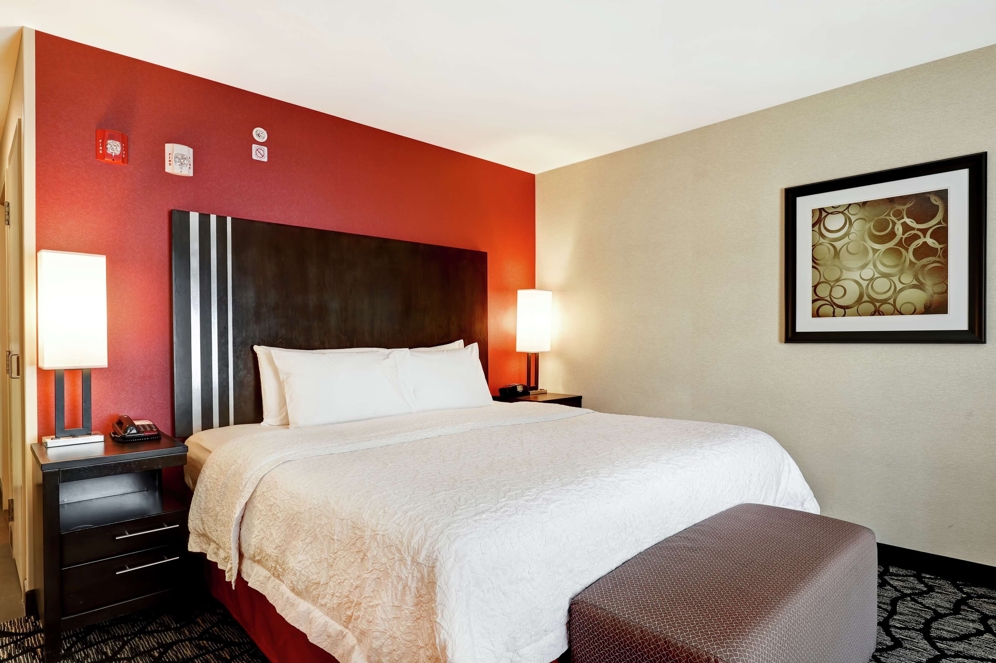 Une chambre d’hôtel avec un grand lit, une table de chevet avec une lampe, un bureau avec un téléphone et une œuvre d’art encadrée au mur.