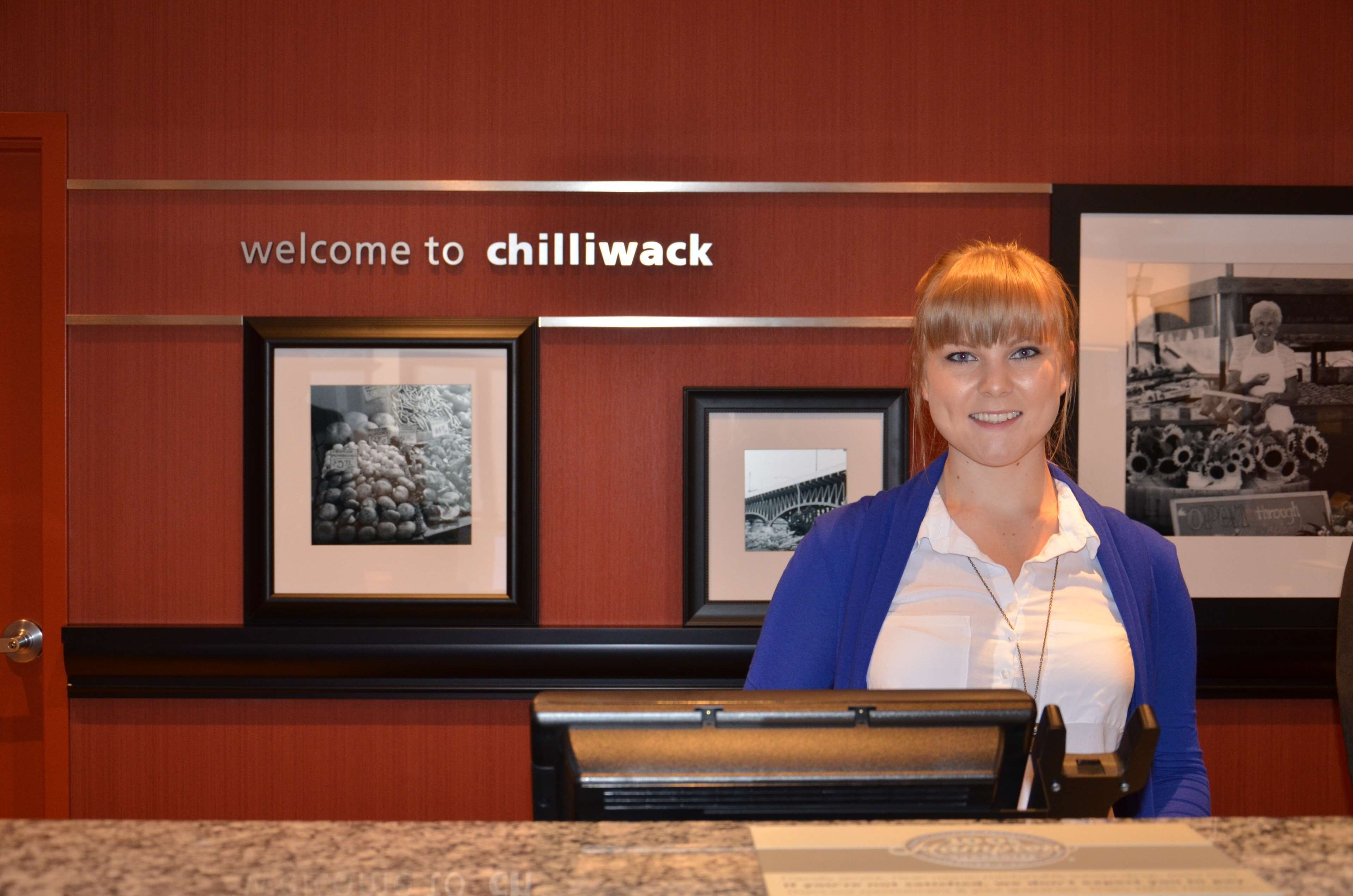 A reception desk with a sign reading "welcome to chillywack" and framed black and white photographs on the wall.