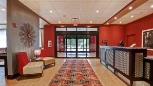 Un vestíbulo de hotel con alfombra roja, un mostrador de recepción y una gran pieza decorativa en la pared.