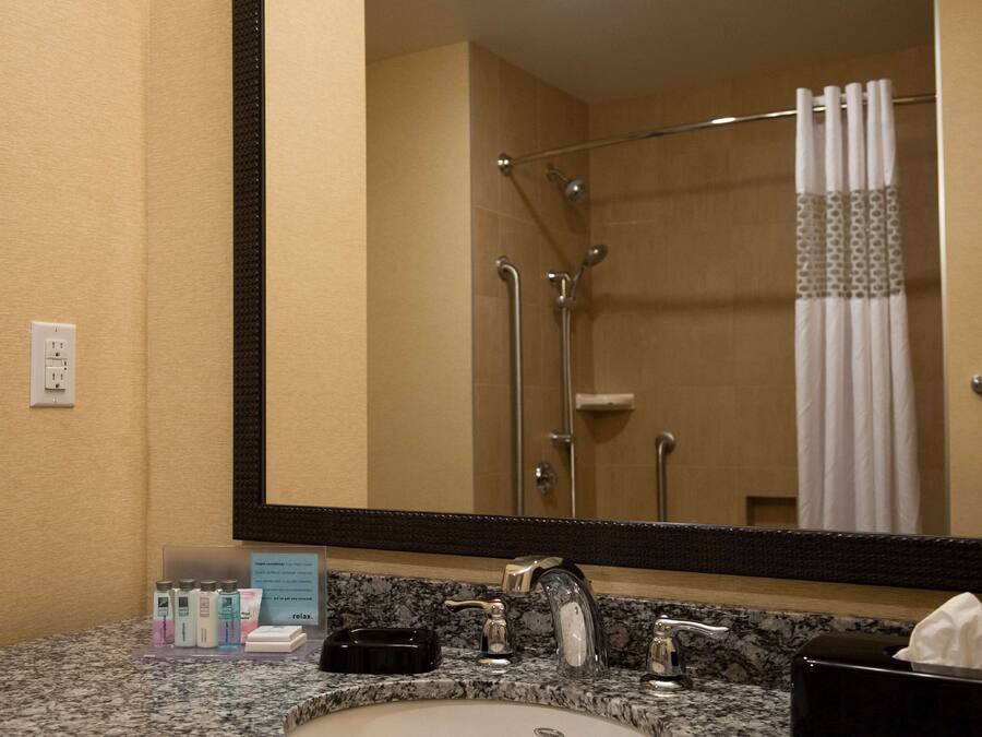 Ein Badezimmer mit Granitplatte, Waschbecken, Spiegel, Duschkabine mit Glastür und Handtuchhalter.