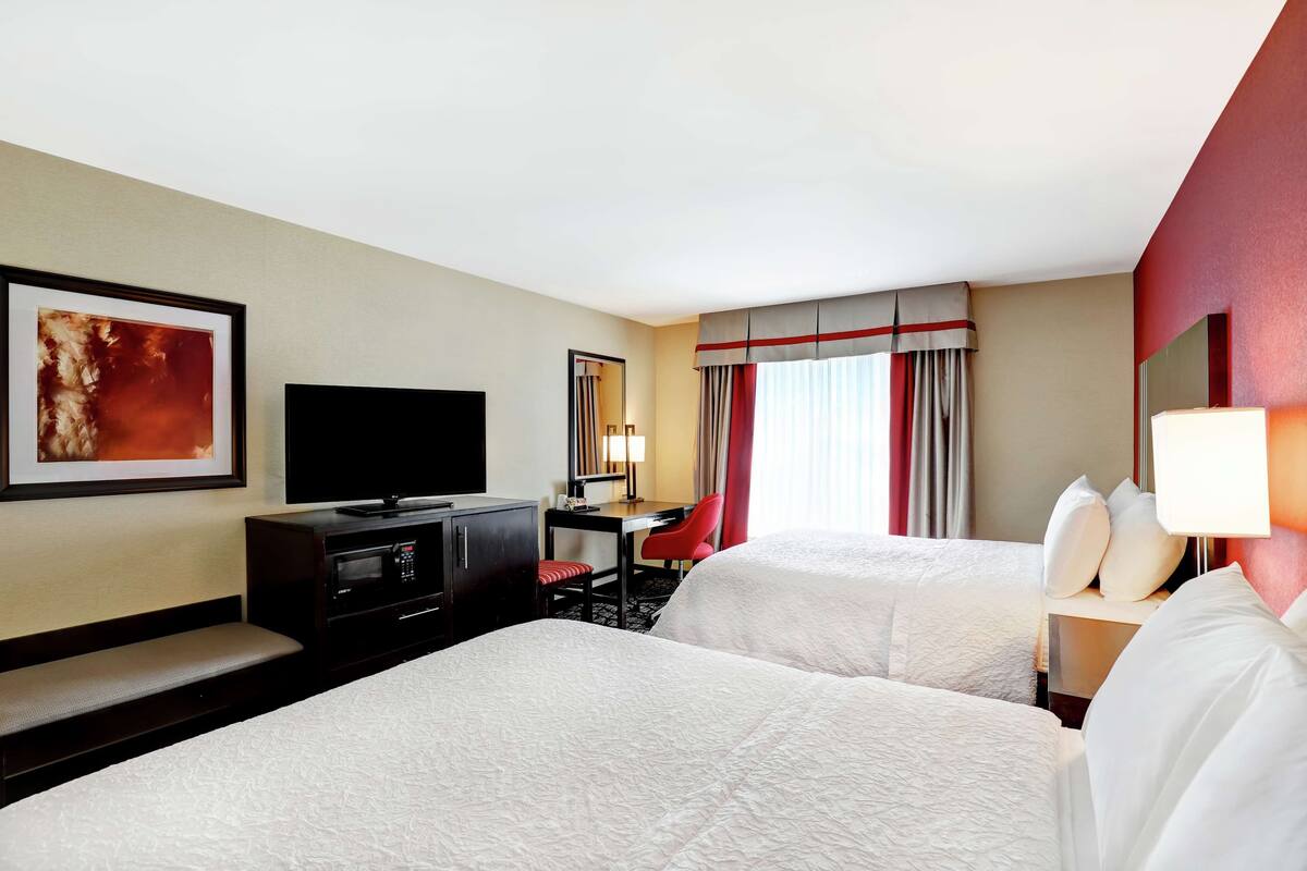 Quarto de hotel com duas camas, uma escrivaninha, uma televisão e um espelho.