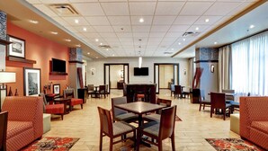 Un vestíbulo de hotel con una mesa de comedor central rodeada de sillas, un televisor montado en la pared y una chimenea.