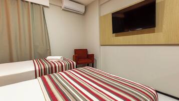 A hotel room with two beds, a TV mounted on the wall, and a chair.